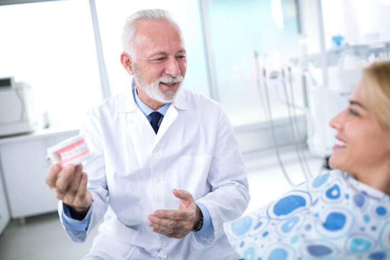 dentist holding teeth to show patient what a dental bridge procedure looks like